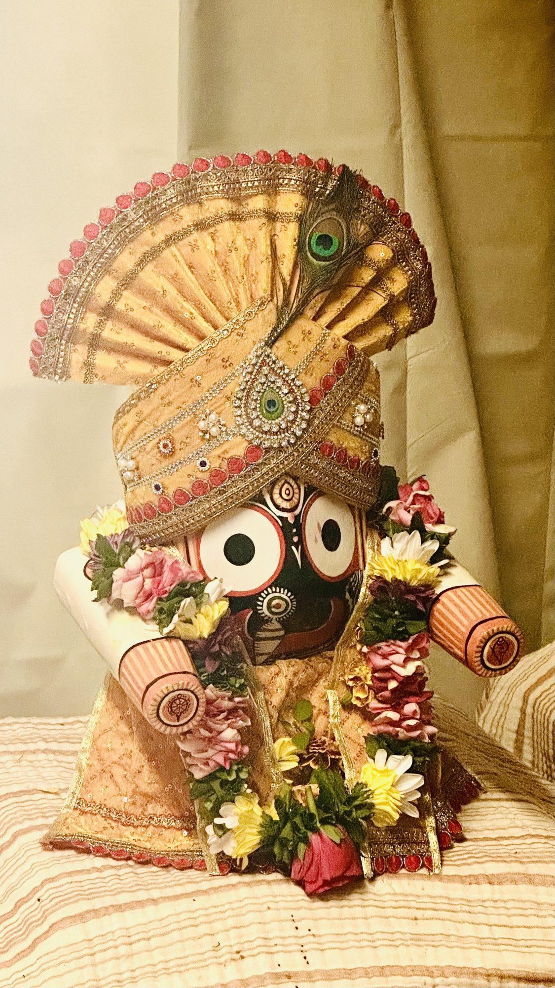 A Jagannath idol with a gold-toned fan-shaped crown, peacock feather and flower garlands